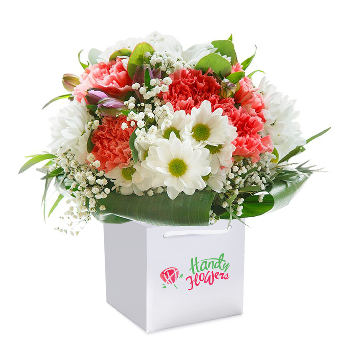 This striking floral arrangement appears freshly prepared by Flower Delivery Malden Rushett, casting a sense of abundance and tranquillity reminiscent of the local countryside. A medley of coral, peach, and deep red carnations stands central, each flower brimming with ruffled petals and inviting textures that carry a natural vibrancy. White daisies adorned with lively golden-green centers pop against their neighbours, bringing a playful freshness much like the wildflower borders lining the meadows near Rushett Lane. Intertwined throughout the bouquet, wisps of baby's breath shimmer with snowy softness, while a handful of purple-tipped buds nestle among the blooms, adding gentle hints of mystery. The entire arrangement is enfolded by glossy, lush green foliage, its broad leaves forming a welcoming base and framing the gathering in leafy luxury. This artistry is thoughtfully nestled into a modern white gift bag, complete with crisp ribbon handles-ready for easy presentation or a doorstep delivery around Malden Rushett or Ashtead Park. Soft studio light bathes the bouquet, highlighting every detail and further enhancing the colours' richness. With its full, rounded form and timeless palette, this image perfectly evokes the joy of gifting flowers-for celebrations, heartfelt thanks, or simply brightening someone's day in the neighbourhood-reflecting the expert craftsmanship synonymous with quality local floristry.