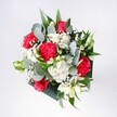 This bouquet appears as a vivid, hand-tied celebration of red and white, the kind of arrangement you might see carried across Malden Rushett on a bright morning. At its heart sit velvety crimson roses, their petals spiralling inward like soft satin, surrounded by ruffled pink-red carnations that bring movement and texture. Clusters of snow-white daisies or chrysanthemums add a daisy-like lightness, each tiny central disk glowing softly against the neat ring of petals. Threaded through the blooms are fine sprays of gypsophila, or baby's breath, forming a gentle white mist that softens the strong colours and gives the whole bouquet an airy halo. Cool eucalyptus stems arc gracefully between the flowers, their rounded leaves a muted blue-green, catching light with a slight silvery sheen. Behind and beneath the main blooms, deeper tropical foliage fans out in rich, glossy greens, framing the design without ever feeling heavy. The flowers seem to be lit by natural daylight, as if placed near a window overlooking the lanes leading to Chessington or the fields beyond Malden Rushett, giving the reds a warm glow and the whites a clean, luminous clarity. The overall structure is rounded and full but not rigid, as though an experienced local florist tied it carefully while letting each stem find its own comfortable place. It feels joyful and welcoming, ideal for a birthday, a homecoming, or a simple thinking of you delivered to a doorstep near Rushett Lane or Fairoak Lane, the bouquet radiating affection, optimism, and the quiet thrill of a special moment marked with fresh flowers.